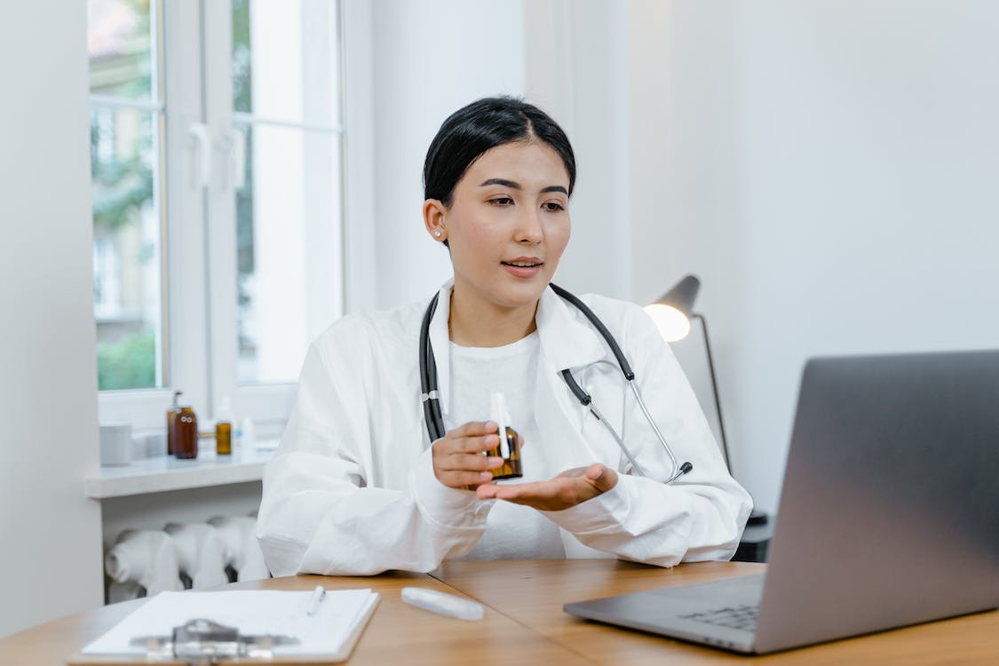 An image of a telemedicine doctor showing a medicine bottle to the patient via a laptop